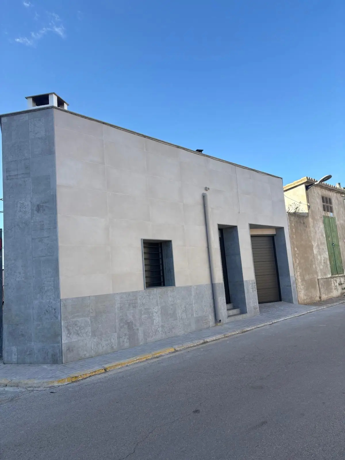 Fachada con revestimiento cerámico en dos tonos de gris y zócalo de piedra en Tarragona