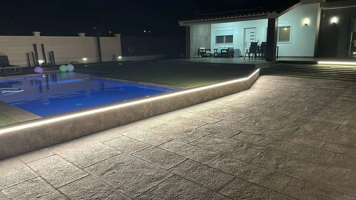 Piscina con iluminación led perimetral en murete de piedra y suelo de gres exterior en Tarragona