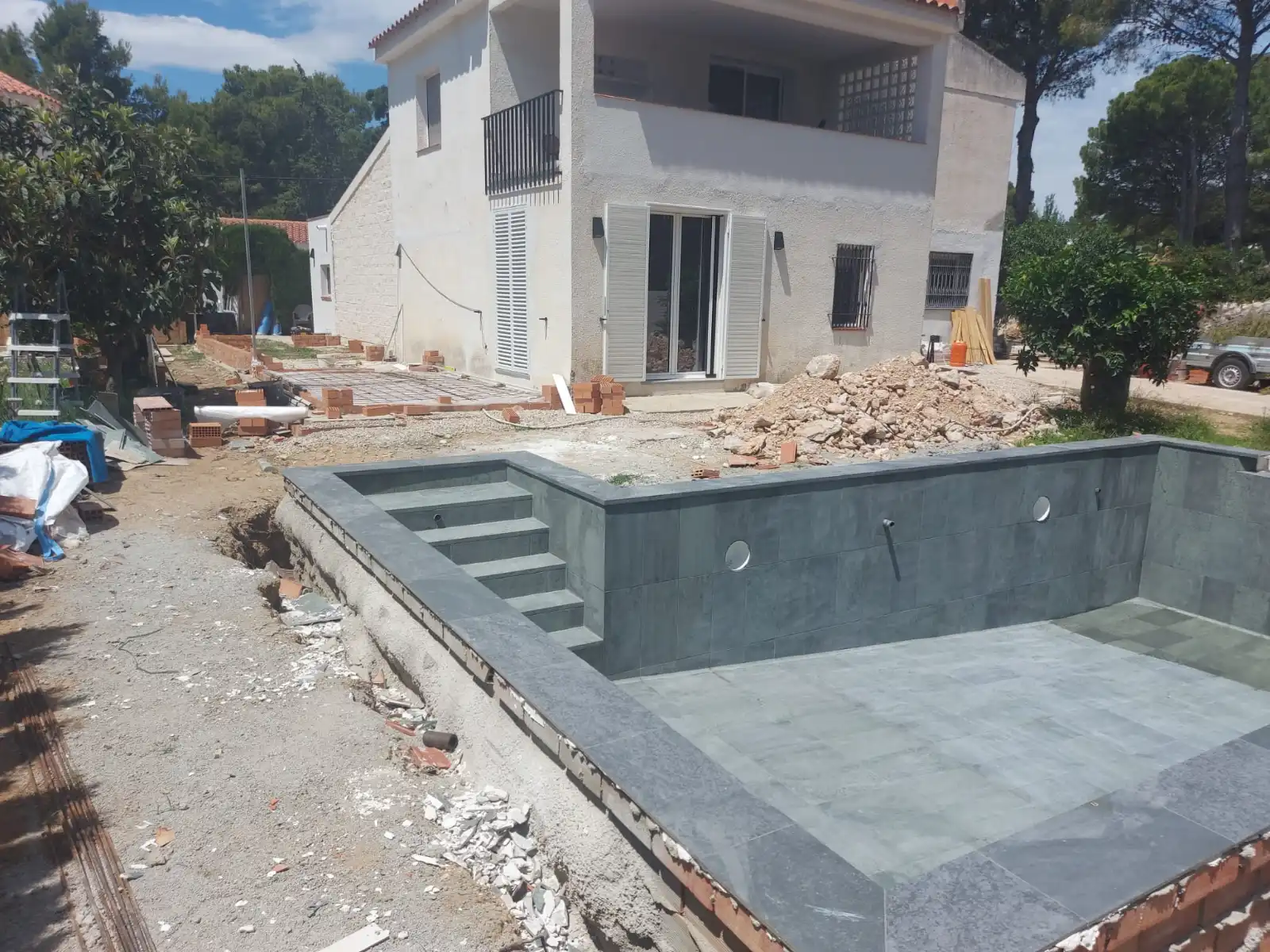 Construcción de piscina con revestimiento de gresite gris oscuro y escalera de obra en Tarragona