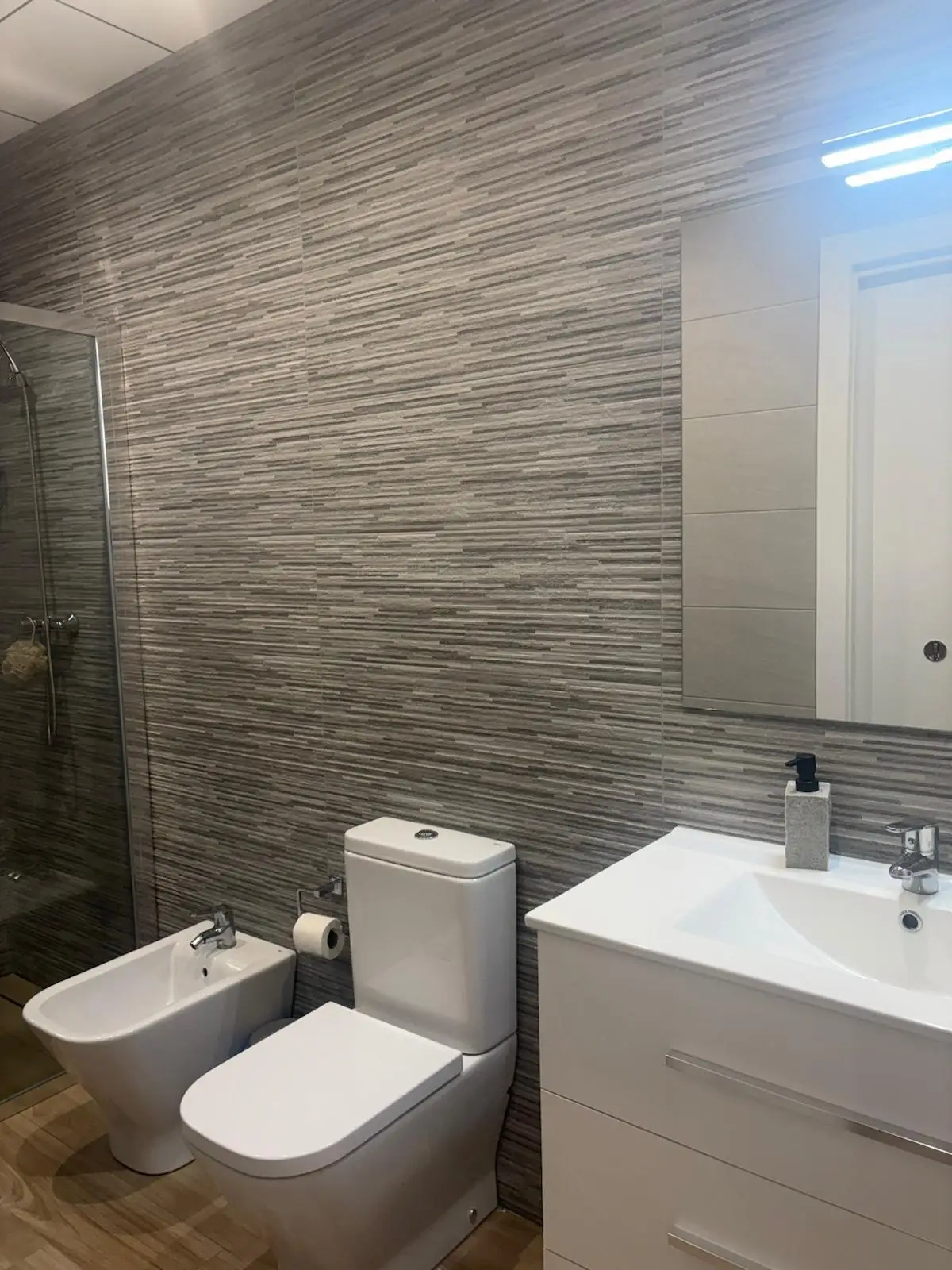Reforma de baño con alicatado de rayas grises, mueble blanco y sanitarios modernos en Tarragona