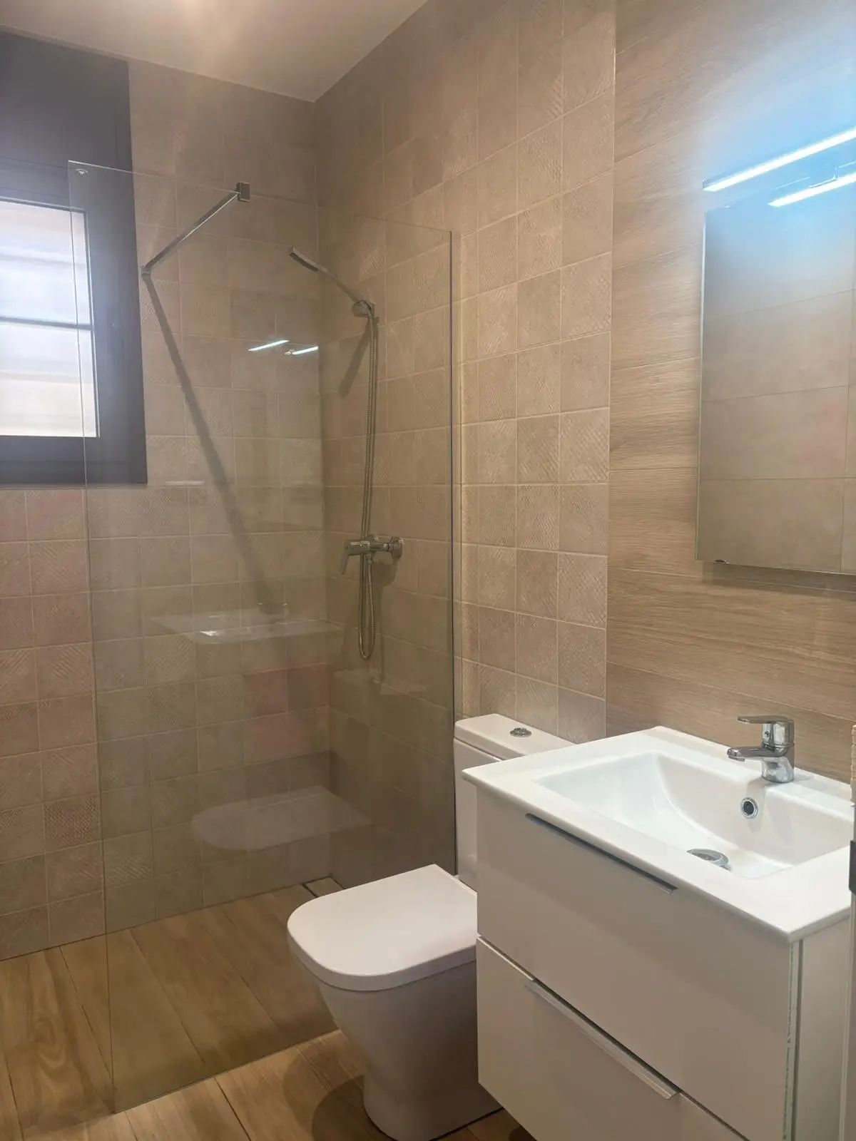 Reforma de baño con mampara de cristal fija, mueble blanco y revestimiento cerámico en Tarragona