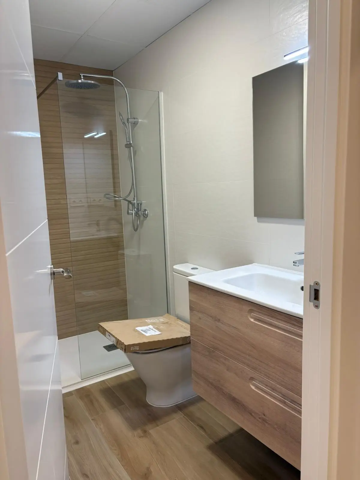 Reforma de baño con mueble suspendido de madera y ducha con mampara de cristal en Tarragona