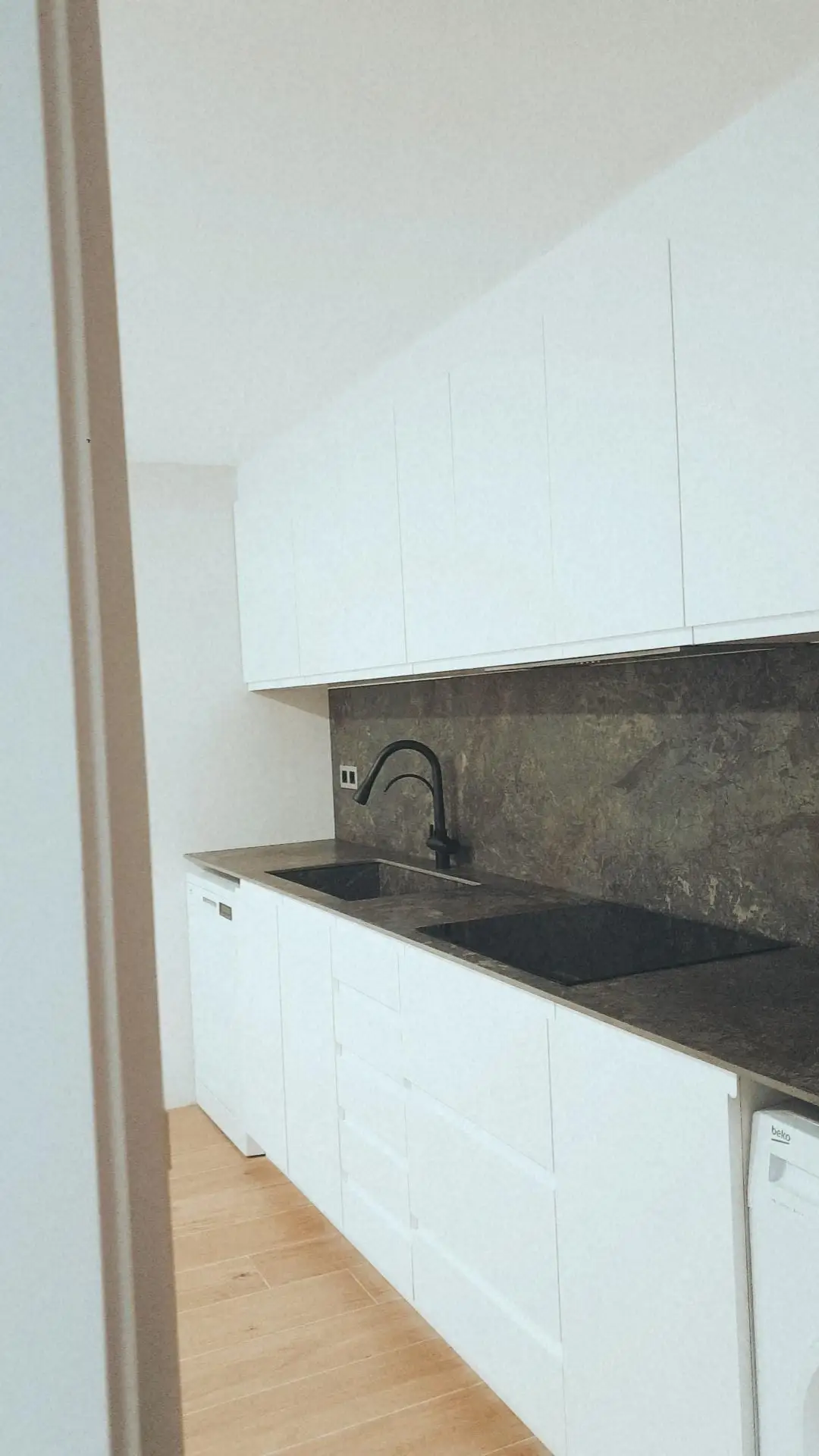 Reforma de cocina con mobiliario blanco minimalista y encimera de piedra oscura en Tarragona