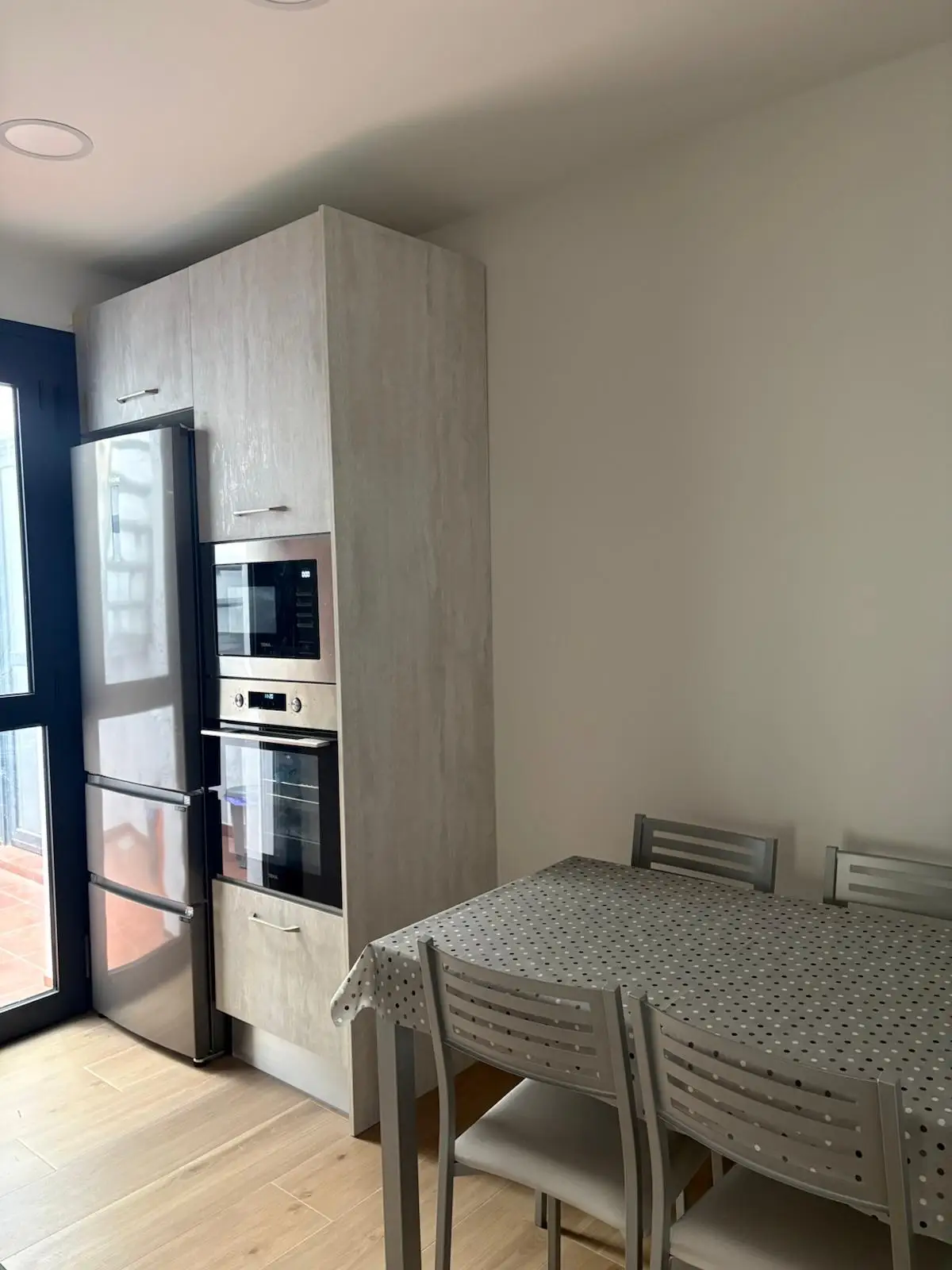 Reforma cocina con columna de hornos, muebles de madera clara y zona de comedor en Tarragona