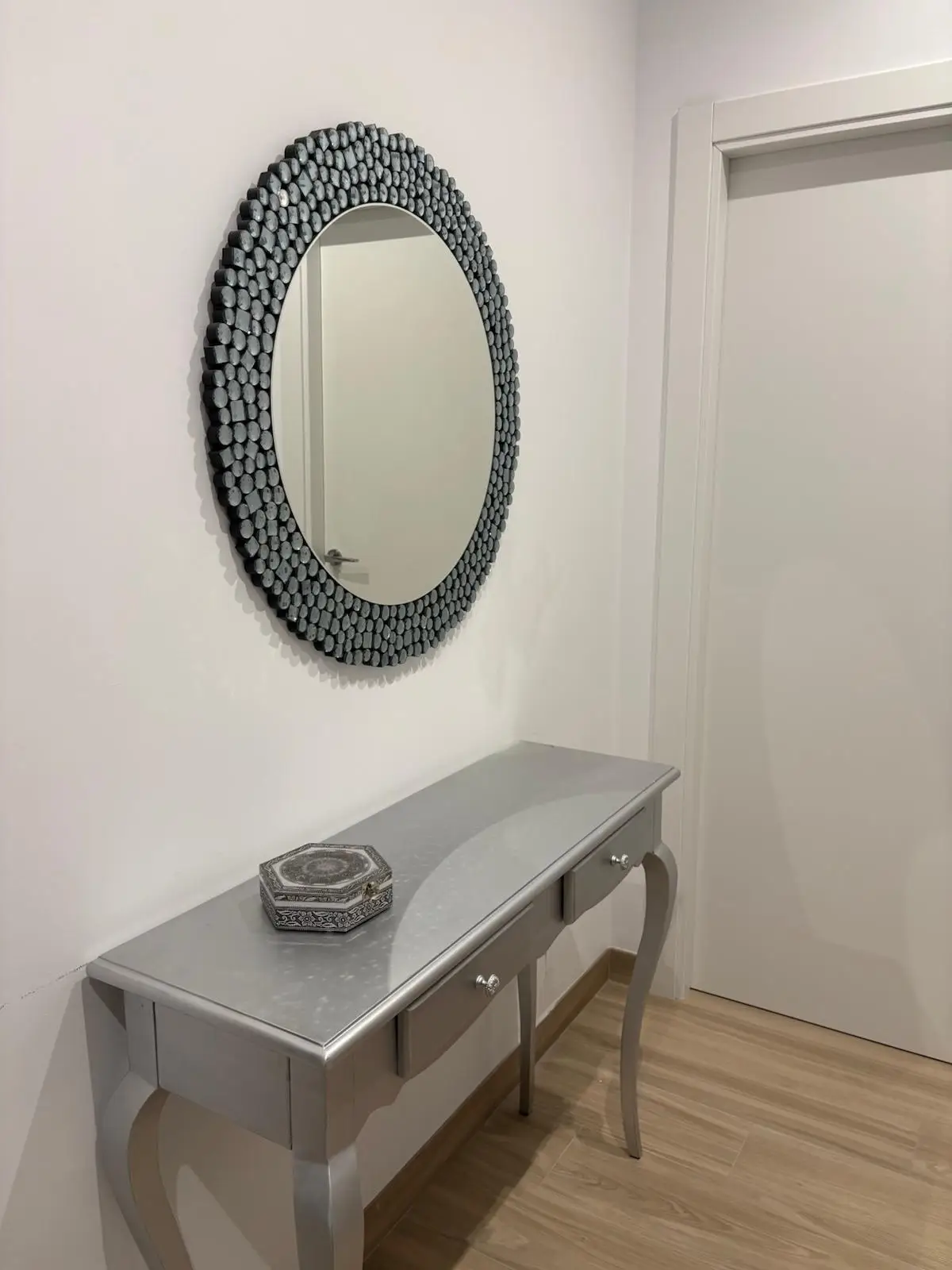 Reforma integral con recibidor de paredes blancas, consola plateada y espejo ovalado decorativo en Tarragona