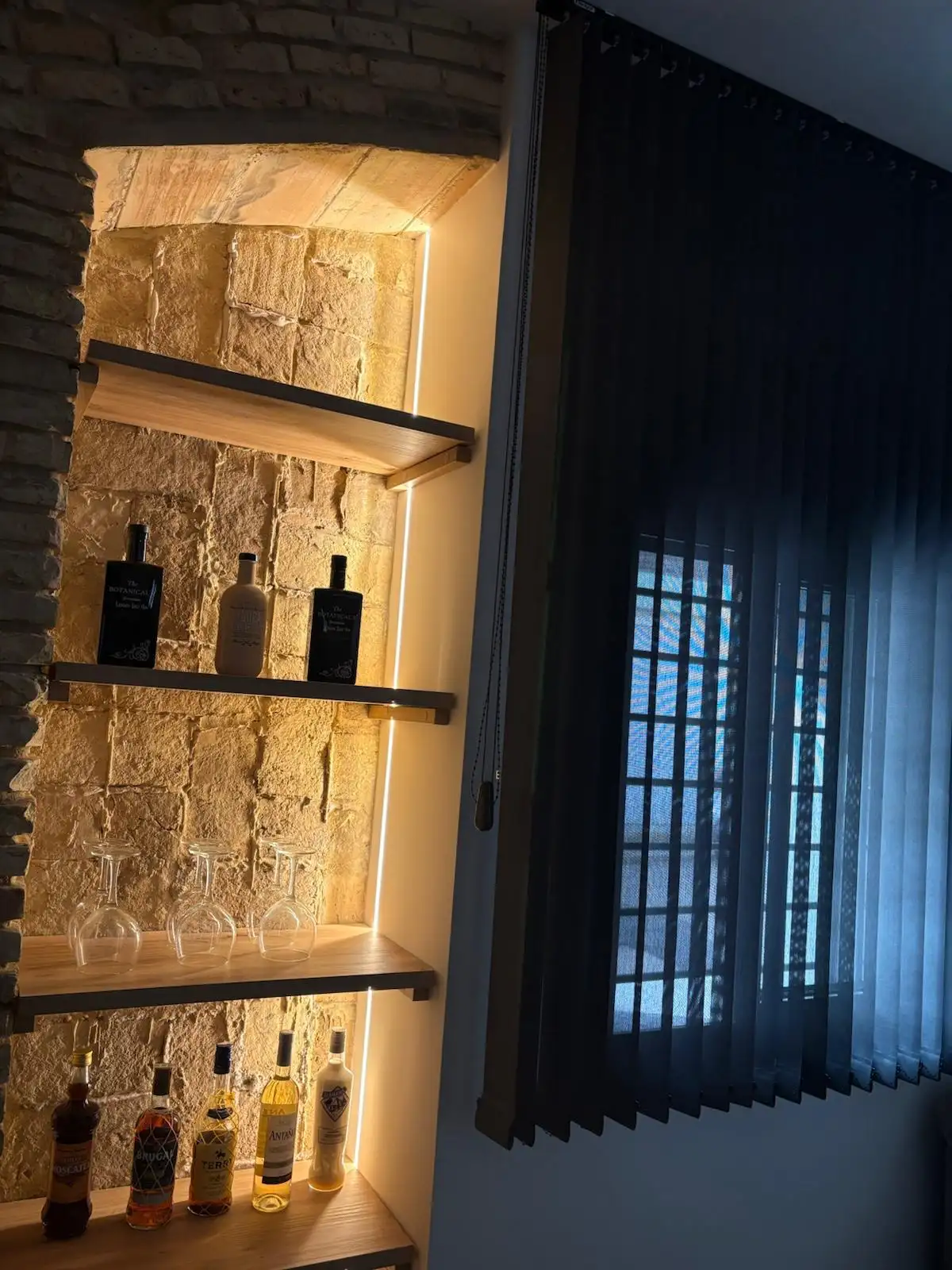 Reforma integral con estantería de madera sobre pared de piedra retroiluminada en una vivienda de Tarragona