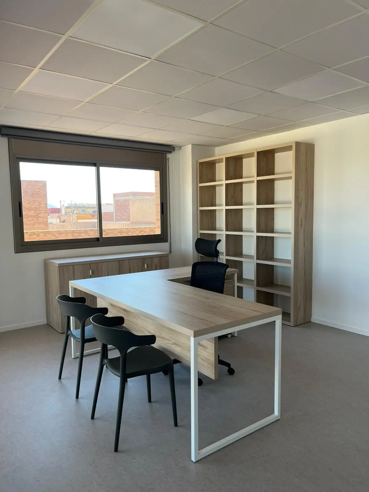 Reforma integral de oficina con mobiliario de madera clara, escritorio en L y estantería en Tarragona