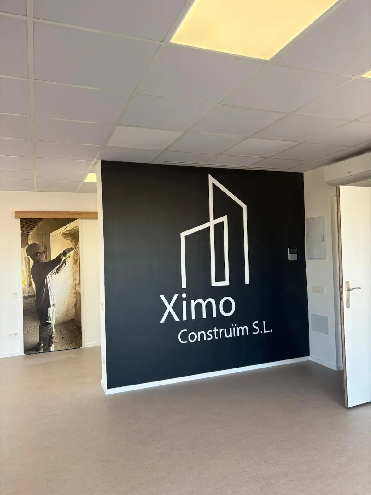 Reforma integral de oficina con pared corporativa negra, logotipo blanco y falso techo en Tarragona