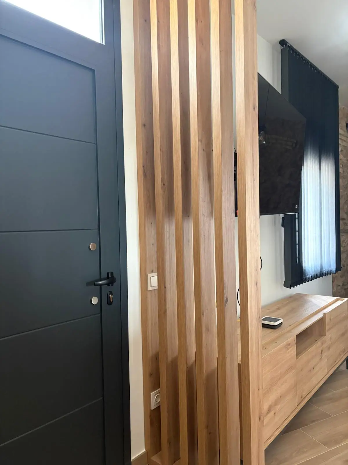 Reforma integral con separador de listones de madera natural y puerta de entrada gris en Tarragona